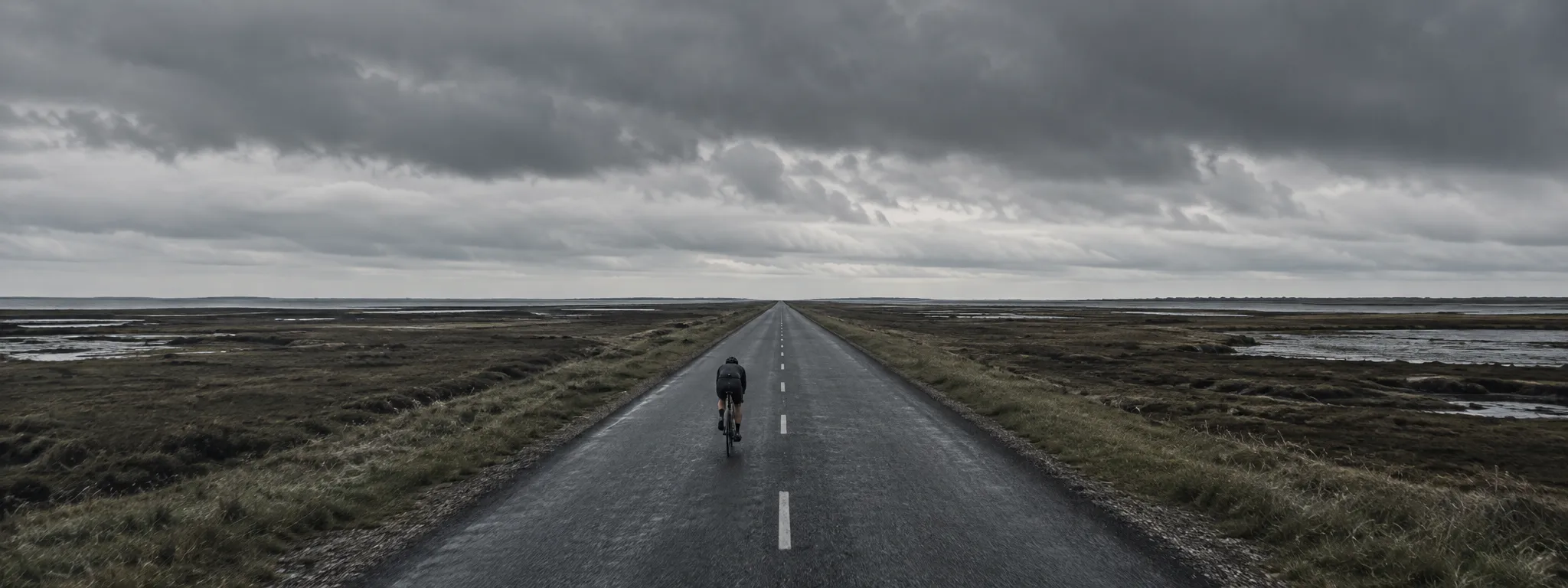 Lone cyclist on a straight empty road running to the horizon under an overcast sky